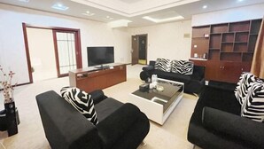 Een moderne woonkamer met een flatscreen televisie, zwarte banken met zebraprint kussens, een salontafel en een houten wandplank.