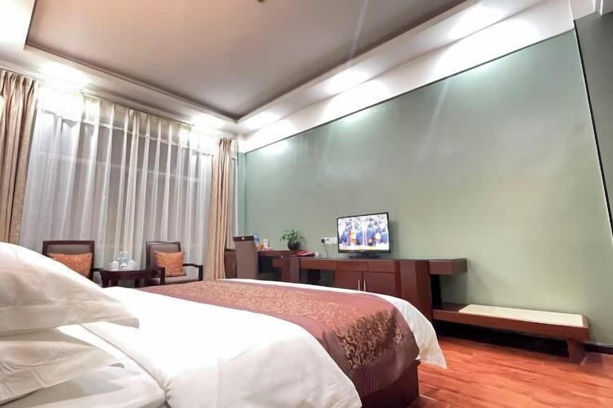 Ein Hotelzimmer mit Bett, Schreibtisch, Fernseher und einem Fenster mit Vorhängen.