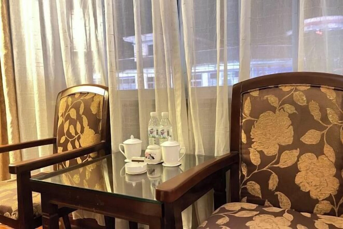 Un coin repas avec une table en verre, deux chaises recouvertes d’un tissu à motifs floraux et une vue dégagée à travers des rideaux légers.