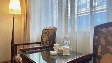 A room with a glass-top table, two chairs, a lamp, and a window with curtains.