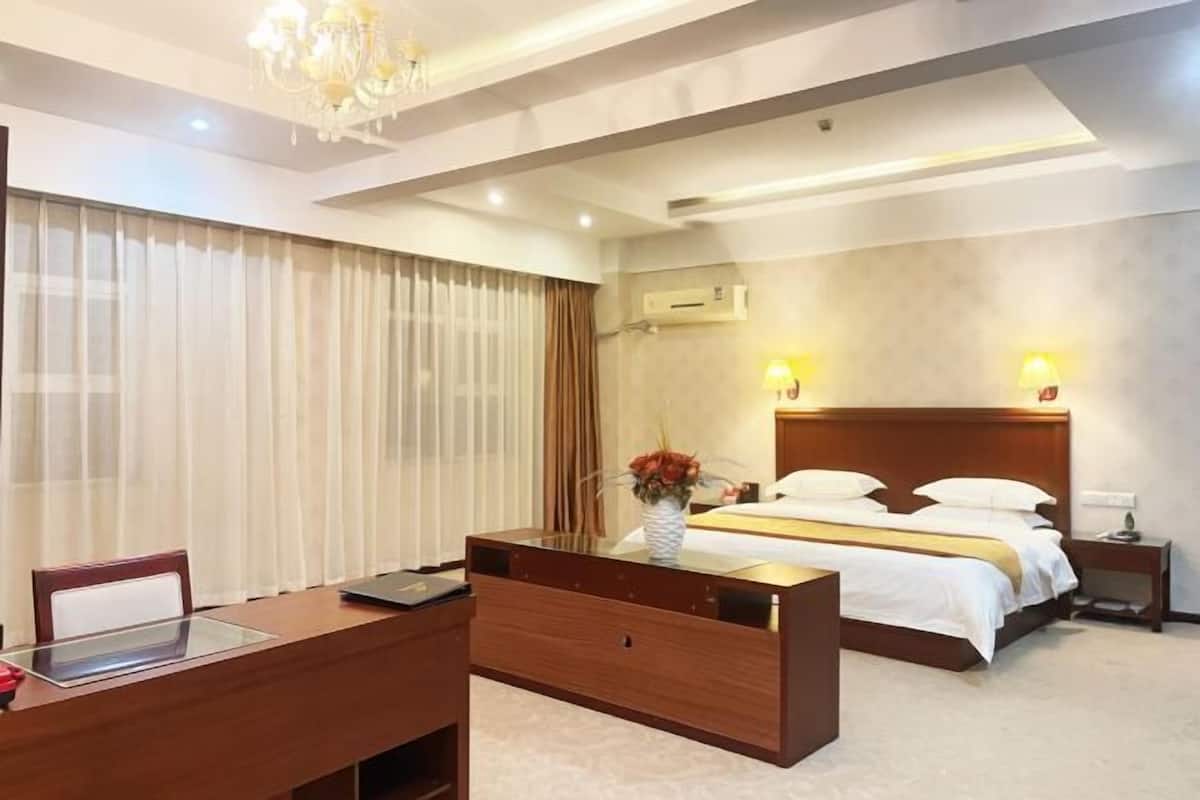 Ein Hotelzimmer mit einem Holztisch, einem Bett mit weißer Bettwäsche, einer Kristallleuchtre und einer Klimaanlage an der Wand.