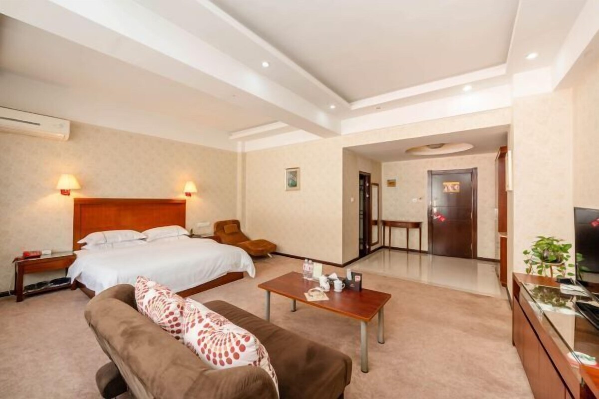 Une chambre d’hôtel avec un grand lit, un canapé, une table basse, une télévision et une salle de bain visible à travers une porte ouverte.