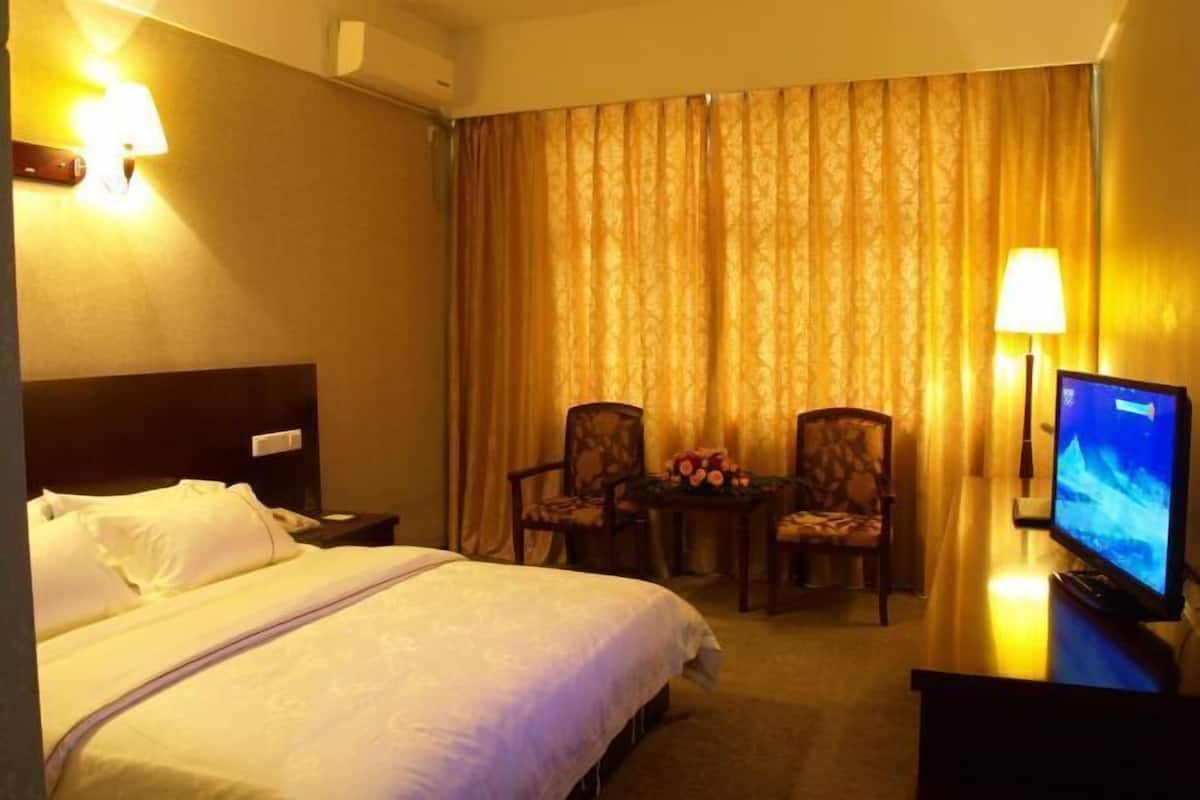 Ein Hotelzimmer mit einem Bett, zwei Stühlen, einem Tisch mit Blumen, einem Fernseher und Vorhängen.