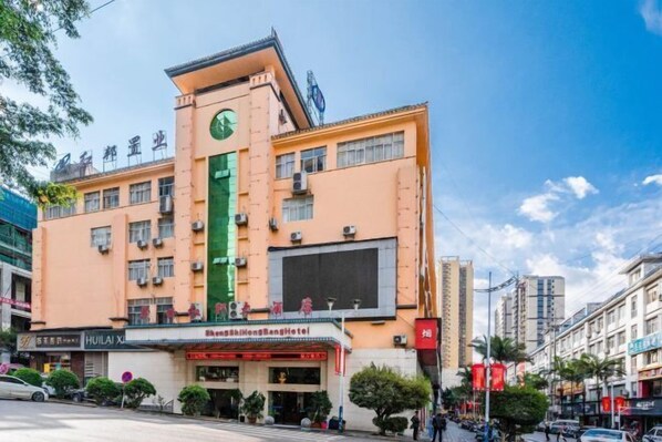 Un hôtel avec une bande verticale verte sur sa façade, de nombreux étages et une tour horloge.