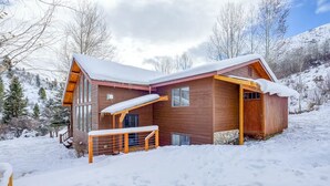 Een houten chalet met een met sneeuw bedekte dak, grote ramen en een houten terras.