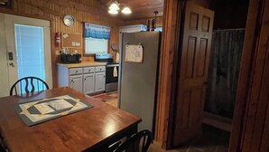 A wooden interior with a dining table, chairs, a refrigerator, and a kitchen area with a stove and microwave. - Lake Front Cabin in Quiet Cove (Stover)