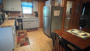A compact kitchen with wooden cabinets, a refrigerator, a sink, and a dining table with chairs. - Lake Front Cabin in Quiet Cove (Stover)