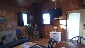 A cozy cabin-style room with a wooden interior, a sofa, a dining table, and a TV mounted on the wall. - Lake Front Cabin in Quiet Cove (Stover)