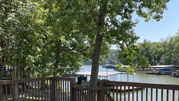 A wooden deck with a picnic table and benches, overlooking a calm lake with boats and a dock in the background. - Lake Front Cabin in Quiet Cove (Stover)
