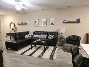 A living room with a sectional sofa, a coffee table, a side table, a lamp, a chair, and a rug. - 3BR/2.5BA Home - 2 Queen+2 Single Bds - North Jax (Jacksonville)