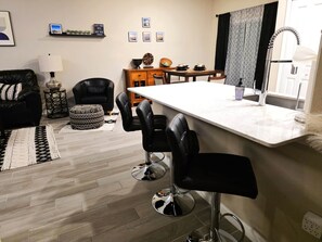 A modern living room with a black leather sofa, a coffee table, and a dining area with a white table and black chairs. - 3BR/2.5BA Home - 2 Queen+2 Single Bds - North Jax (Jacksonville)