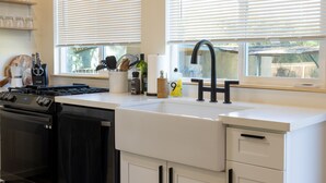 Uma cozinha moderna com armários brancos, fogão preto e janela com persianas.