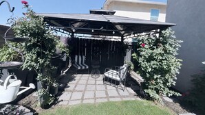 Een overdekt terras met een zithoek, een barbecue en plantenpotten.