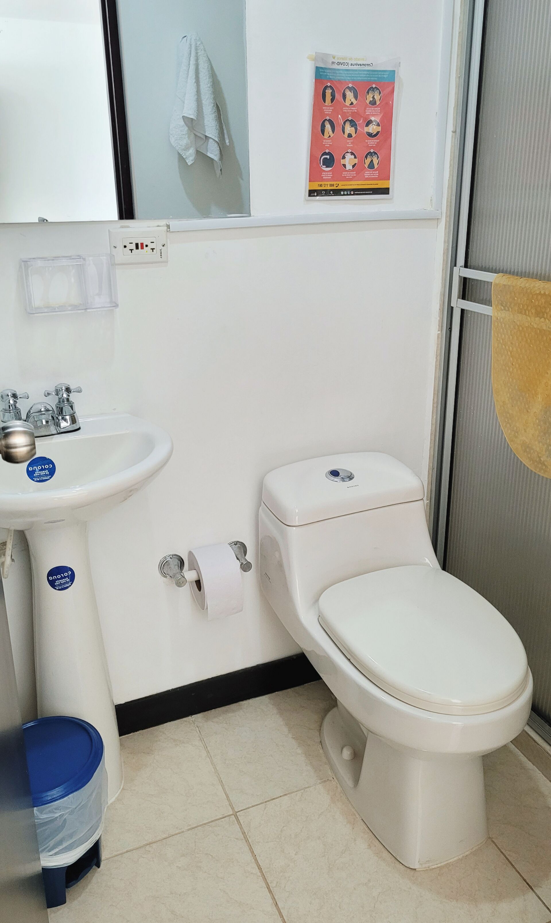 Een badkamer met een witte wastafel, toilet en een blauwe prullenbak.