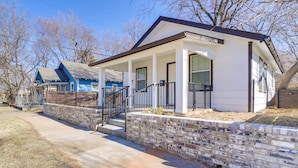 A single-story house with a front porch, a stone retaining wall, and a clear blue sky. - Convenient Tulsa Home - 2 Mi to Downtown! (Tulsa)