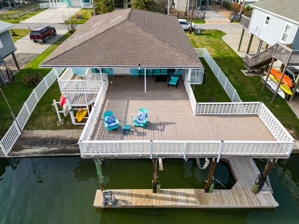 Ein Haus mit einem Steg, der sich ins Wasser erstreckt, mit einer überdachten Terrasse, auf der Stühle und ein Tisch stehen.