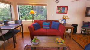 A living room with a red sofa, a wooden coffee table, and a dining area with a table and chairs. - Private Edmonds Studio Apartment (Edmonds)
