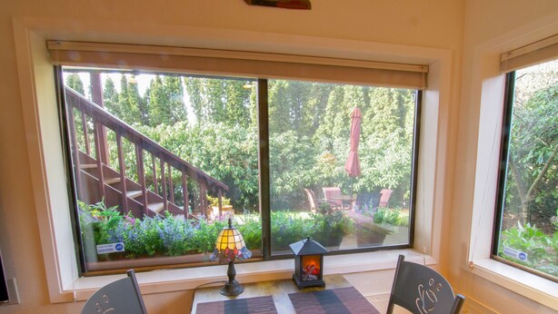 A dining area with a table and chairs, a decorative lamp, and a view of a garden through a large window. - Private Edmonds Studio Apartment (Edmonds)
