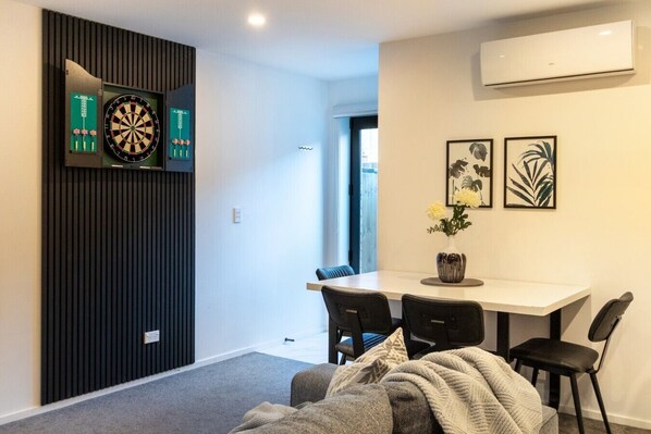Un salon moderne comprenant un coin repas, un jeu de fléchettes et des œuvres d’art encadrées accrochées au mur.