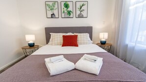 A neatly made bed with a red pillow, two bedside lamps, and three framed plant artworks on the wall. - 2 Bedroom Central Christchurch Hub (Christchurch)