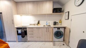 A compact kitchen with wooden cabinets, a built-in oven, a washing machine, and a microwave. - 2 Bedroom Central Christchurch Hub (Christchurch)