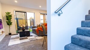 A modern living room with a sofa, coffee table, and a large plant. - 2 Bedroom Central Christchurch Hub (Christchurch)