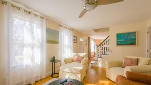 A spacious living room with a ceiling fan, a staircase leading to another level, and a painting on the wall. - Nature Lover's Pondside Getaway (Mashpee)