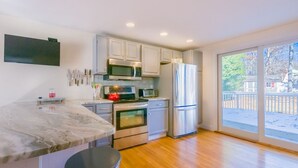 A modern kitchen with a marble countertop, stainless steel appliances, and a large sliding glass door to the outdoors. - Nature Lover's Pondside Getaway (Mashpee)
