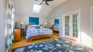 A bedroom with a bed, a ceiling fan, a window, a mirror, and a door. - Nature Lover's Pondside Getaway (Mashpee)