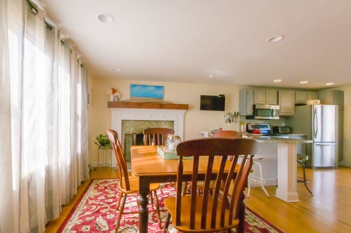 A dining area with a wooden table and chairs, a kitchen with modern appliances, and a fireplace.