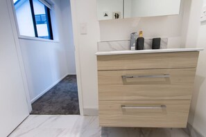 Un baño moderno con tocador blanco, dos cajones y un espejo arriba.