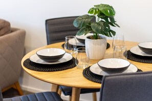 Una mesa redonda de madera con individuales negros, platos blancos y cuencos negros. Una planta en maceta con hojas verdes grandes está sobre la mesa.