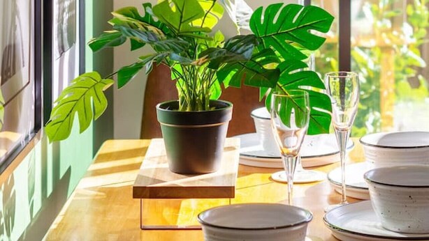 Una mesa de comedor preparada con platos, vasos y una planta en maceta.