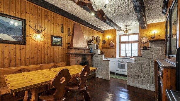 Un intérieur rustique en bois, avec une table et des chaises en bois, une cheminée en pierre et un coin cuisine équipé d’une cuisinière et d’un four.