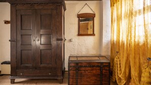 Une pièce avec une grande armoire en bois, une petite commode, un miroir au mur et des rideaux jaunes.