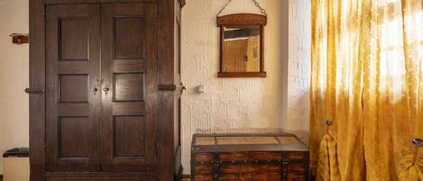 A room with a large wooden wardrobe, a small chest, a mirror on the wall, and yellow curtains.