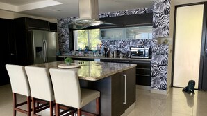 A modern kitchen with a central island, black and white patterned backsplash, stainless steel appliances, and a large window. - Incredible condo with panoramic views of the sea and mountains (Puerto Vallarta)
