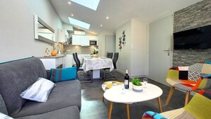 Ein modernes Wohnzimmer mit einem grauen Sofa, bunten Stühlen, einem weißen Couchtisch und einem Essbereich mit weißem Tischlein.