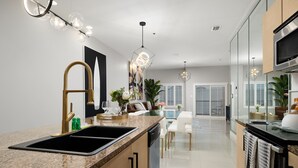 A modern kitchen with a granite countertop, stainless steel appliances, and pendant lighting. - Elegant Condo with Bay Views, Pool & Hot Tub - Walk to Beach! (South Padre Island)