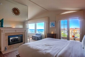 A hotel room with a large bed, a fireplace, a balcony with a view, and a dining area.