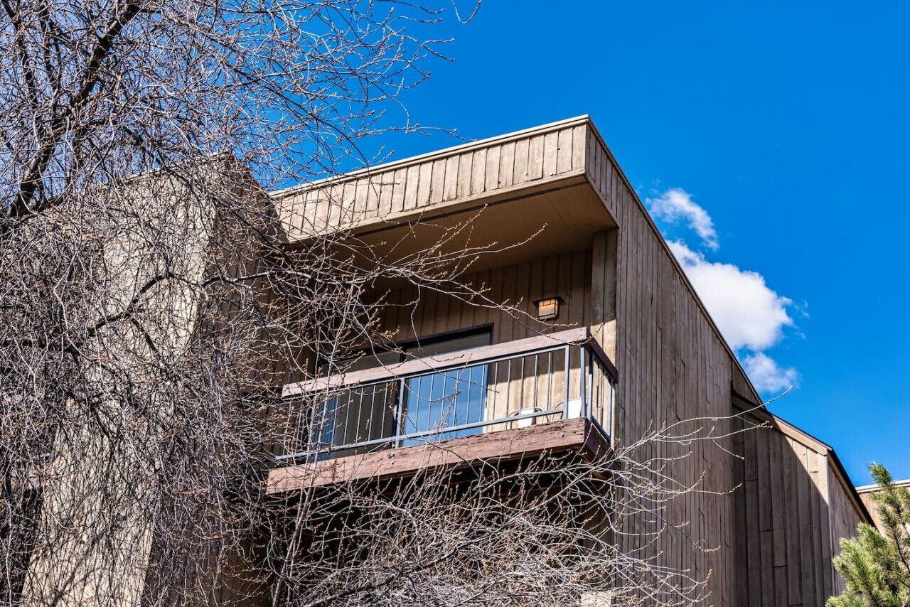 A modern two-story building with a wooden exterior and a balcony with a metal railing.