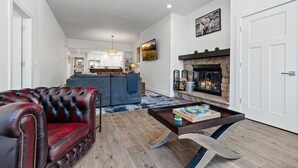 A modern living room with a leather sofa, a coffee table, a fireplace, and a kitchen in the background. - Cozy 3BD/2BA Mt. Condo Overlooking Eagle River (Avon)
