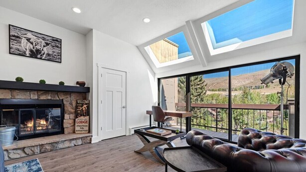A modern living room with a fireplace, leather sofa, and a large window offering a view of the outdoors. - Cozy 3BD/2BA Mt. Condo Overlooking Eagle River (Avon)