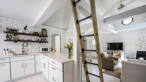 Une cuisine moderne avec des meubles blancs, un îlot central et une échelle en bois appuyée contre le mur.