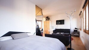 A modern hotel room with a large bed, a sofa, a TV, and a coat rack. - Diamond Penthouse & Terrace (Barcelona)