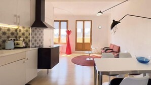 A modern kitchen with a black range hood, a dining area with a white table and chairs, and a red chair in the background. - Diamond Penthouse & Terrace (Barcelona)