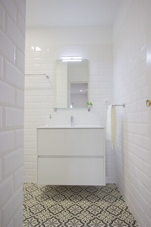 Une salle de bain avec des carreaux de métro blancs, un meuble-lavabo blanc avec un miroir et des carreaux de sol à motifs.