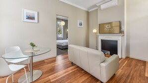 Una sala de estar moderna con una mesa de comedor de vidrio, sillas blancas, un sofá, una chimenea y cuadros en las paredes.
