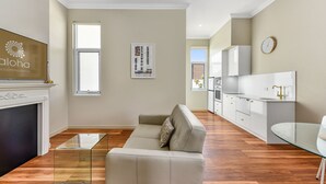 Una sala de estar moderna con un sofá, una mesa de centro de vidrio y una chimenea. Hay una zona de cocina con gabinetes blancos y una mesa de comedor.