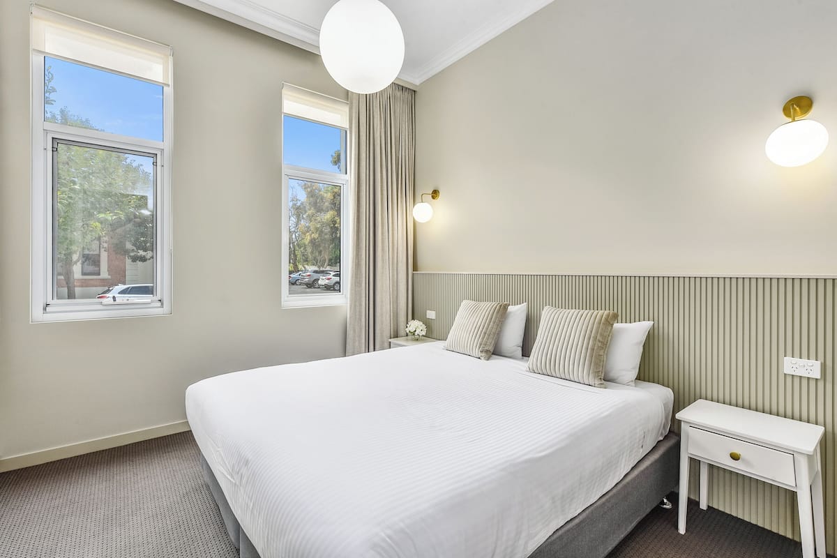 A neatly arranged bedroom with a large bed, two bedside tables, and a window with curtains.